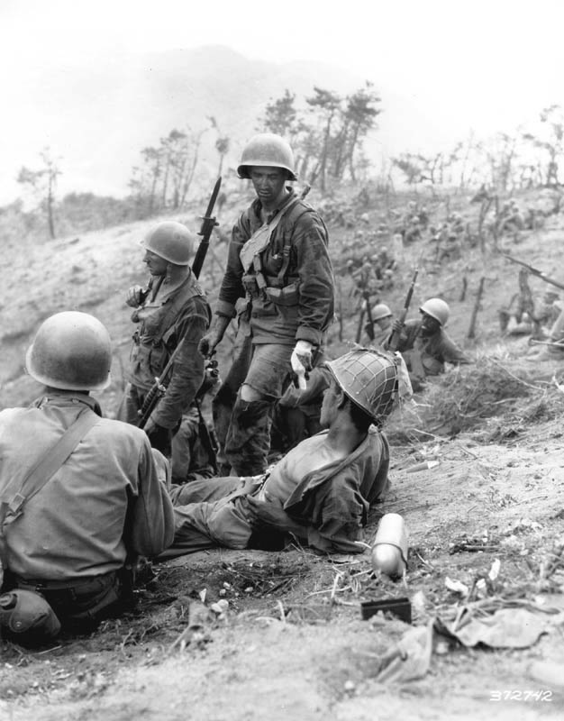 Hit in the back during a grenade duel, Corporal Dominick F. Zegarelli, (Utica, N.Y.) Company L, 7th Regimental Combat Team, U.S. 3rd Infantry Division, waits for evacuation, while other members of his platoon rest. 3 July 1951. Korea. Photo from U.S. Army Signal Corps archive. Photo #8A/FEC-51-23550 (Brigham).” Photo from U.S. Army